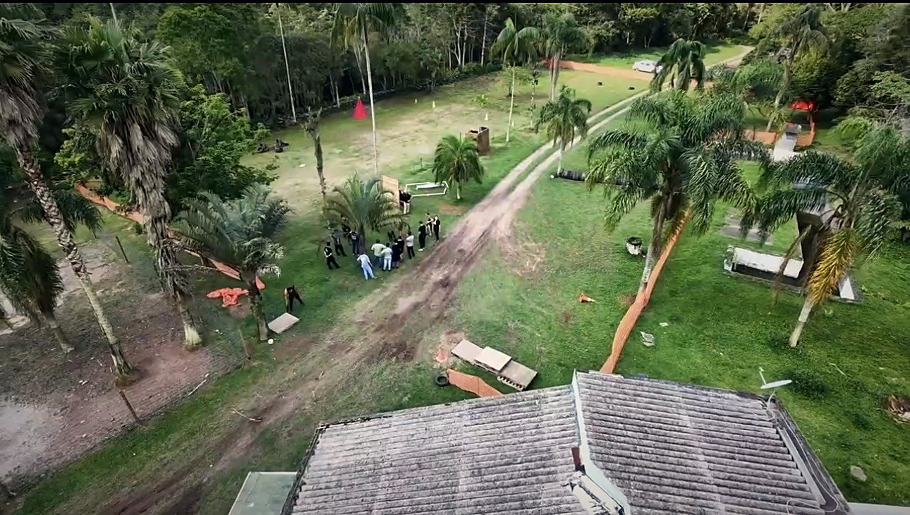 Vista aérea do campo de treino com gramado, cerca laranja e pessoas reunidas